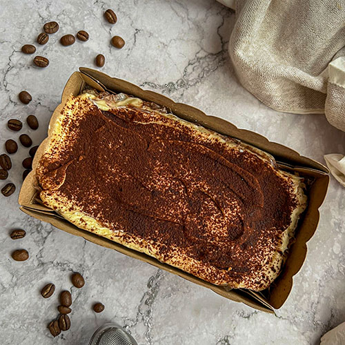 Tiramisu sin gluten de dulces free en una mesa de mármol con unos granos de cafe